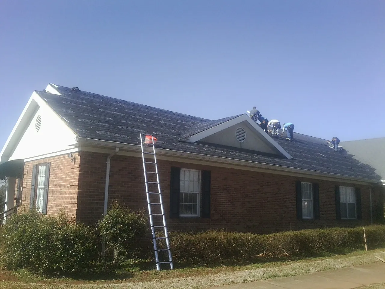 Crew tearing shingles off a brick ranch roof with a ladder set — Emergency Roof Repair work by our crew in Franklinton