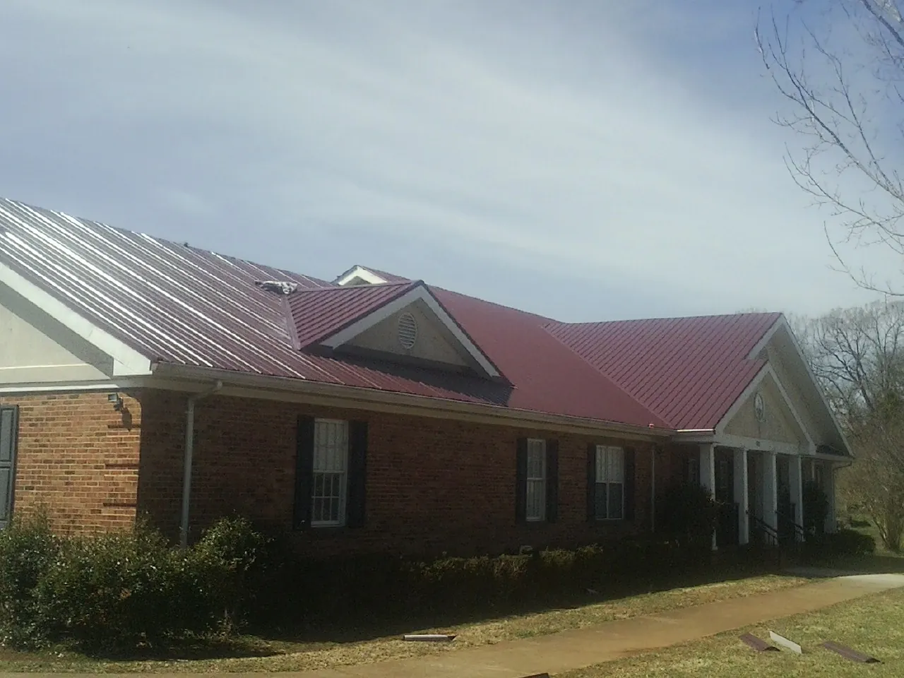 Red metal roof with gabled entries on a long brick building, from a Hail Damage Roof Repair job in Franklinton