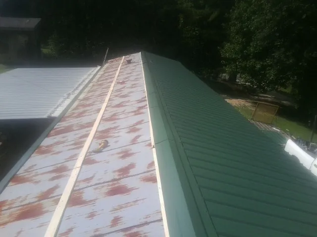 Old rusted panels beside newly installed green metal roofing — Wind Damage Roof Repair by Roofing Brothers in Franklinton