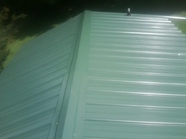 New green metal panels meeting at the ridge of a roof — Flat Roof Repair work by our crew in Franklinton