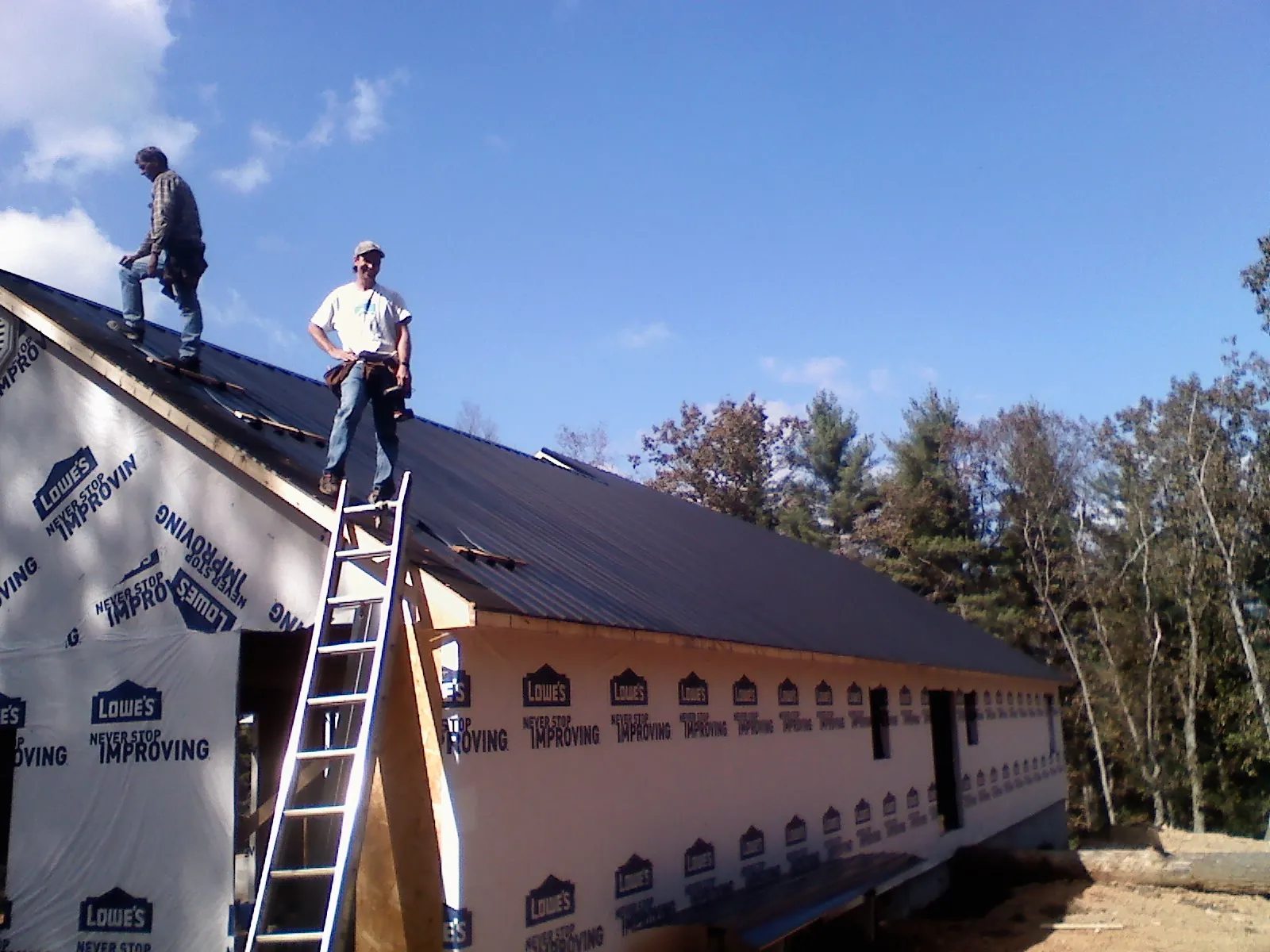Two roofers standing on a long dark metal roof over a wrapped building in Franklinton